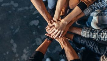 Top view of creative professionals putting their hands together as a symbol of teamwork, cooperation and unity. Stack of hands of men and woman.